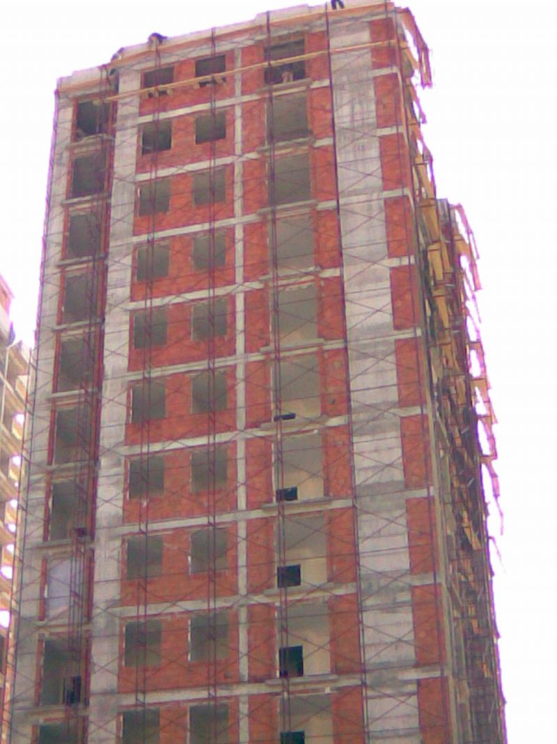 İskele ile çevrili, tuğla ve beton cepheli çok katlı bir bina, alttan yukarıya doğru çekilmiş görünüm